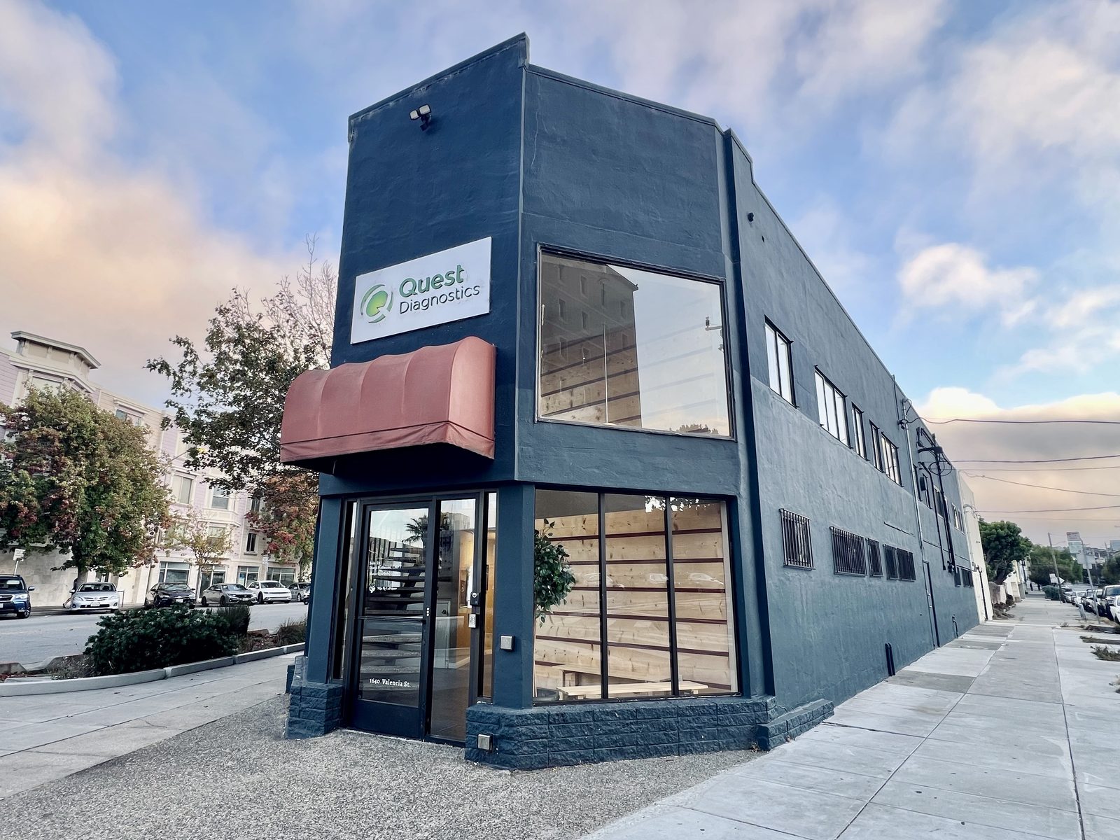 The dark blue corner building at 1640 Valencia St, with a red awning over the street-level entrance